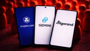 Drei Smartphones mit den Logos von Krypto-Unternehmen vor einer Ansammlung von Figuren