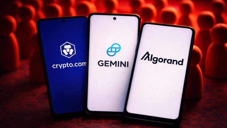 Drei Smartphones mit den Logos von Krypto-Unternehmen vor einer Ansammlung von Figuren