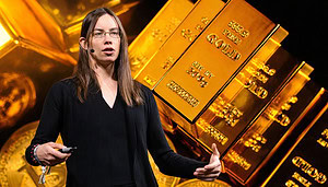 Makroökonomin Lyn Alden vor Goldbarren und Bitcoin-Münzen bei einem Vortrag.