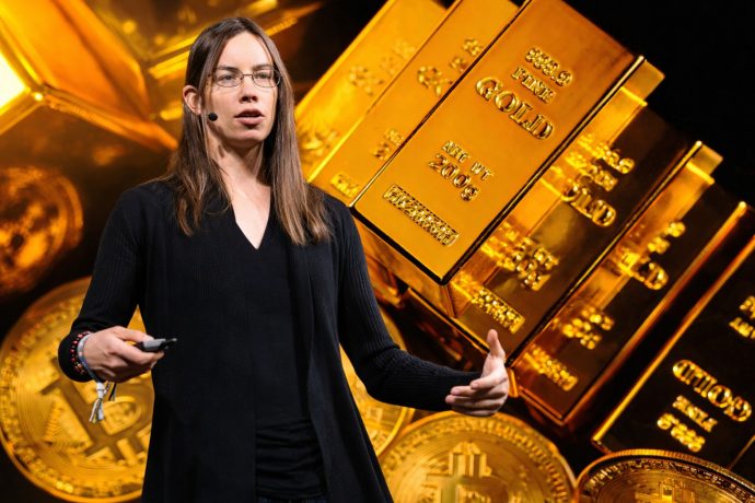 Makroökonomin Lyn Alden vor Goldbarren und Bitcoin-Münzen bei einem Vortrag.