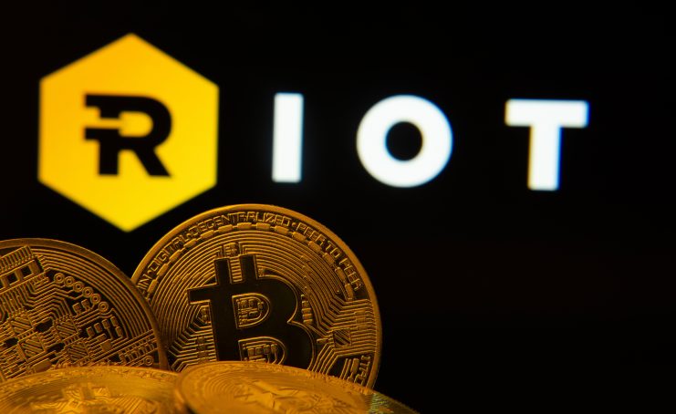 Logo von RIOT, davor Bitcoin-Münzen