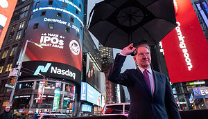 Das Bild zeigt eine Straßenszene in New York am Times Square bei Regen. Im Vordergrund steht ein Mann im Anzug, der einen aufgespannten schwarzen Regenschirm über sich hält.