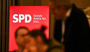 Eine unscharfe Menschengruppe unterhält sich vor dem SPD-Parteilogo.