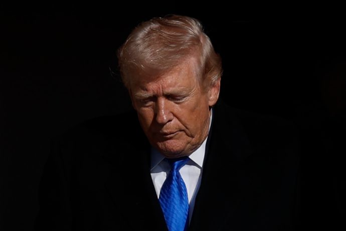 Donald Trump vor schwarzem Hintergrund mit blauer Krawatte.