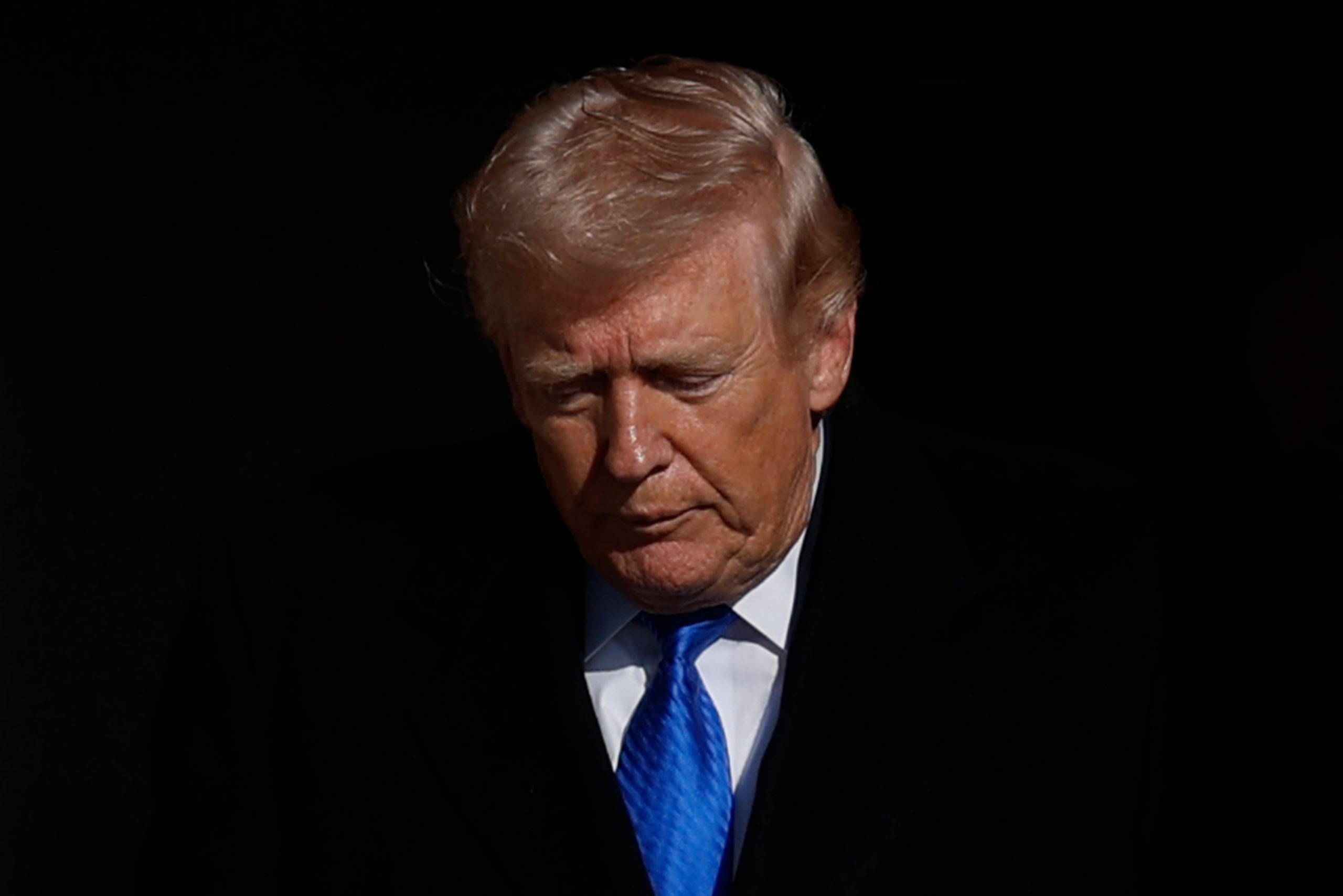 Donald Trump vor schwarzem Hintergrund mit blauer Krawatte.