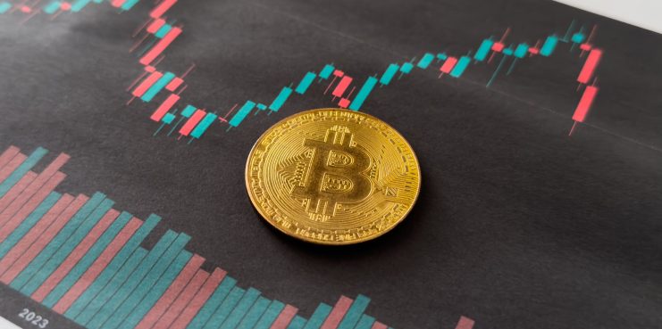 Eine Bitcoin-Münze vor einem Kerzen-Chart.