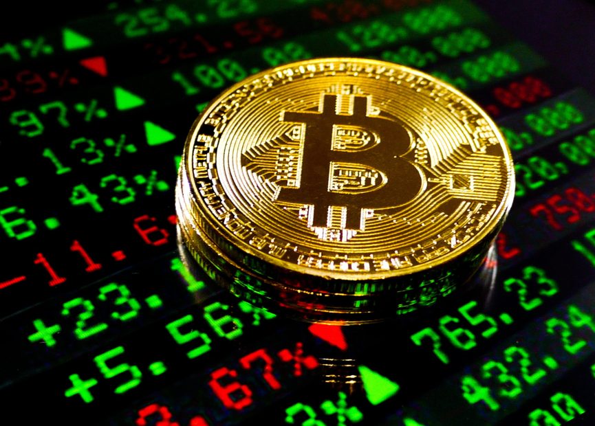 Das Bild zeigt eine Bitcoin-Münze auf einem Bildschirm mit Kurszahlen.