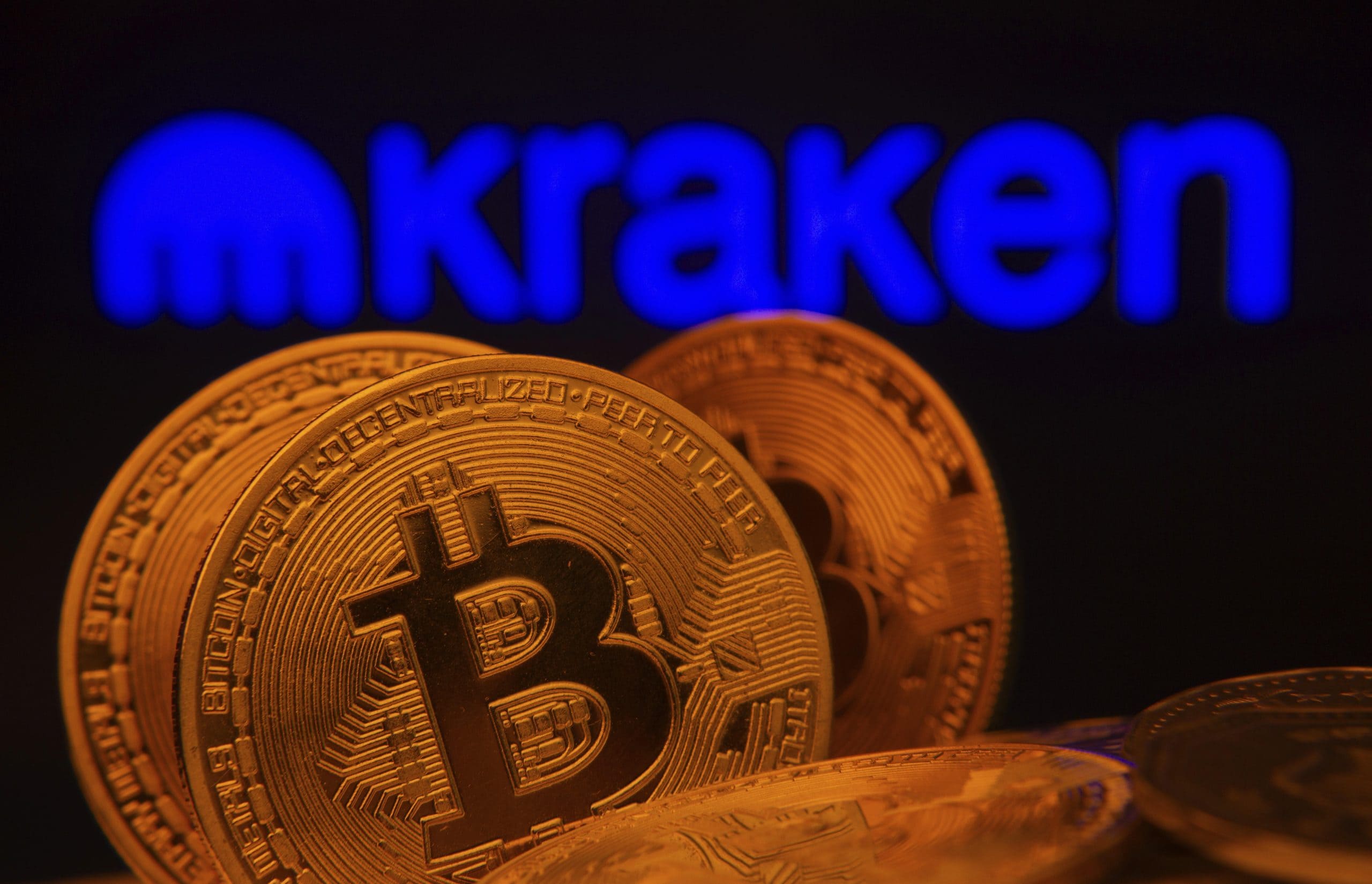 Das Bild zeigt Bitcoin Münzen vor dem Kraken Logo