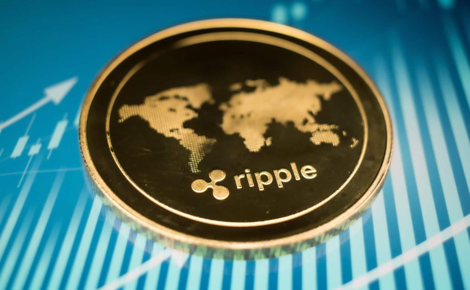 Eine Nahaufnahme einer goldenen Ripple (XRP)-Kryptowährungsmünze mit einem Weltkartenmotiv auf blauem Hintergrund mit Finanzdiagrammlinien.
