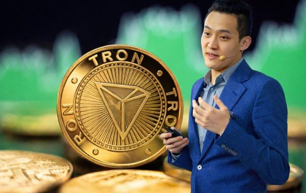 Tron-Gründer Justin Sun vor einer großen TRX-Münze mit Kursgrafik im Hintergrund.