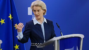 Eine Frau steht auf einem Podium mit der Flagge und dem Emblem der Europäischen Union im Hintergrund. Sie gestikuliert mit ihrer linken Hand und spricht über europäische Krypto-Regulierung und Bitcoin.