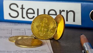 Ein paar vergoldete Bitcoin-Münzen vor einem Aktenordner mit der Aufschrift Krypto-Steuern.