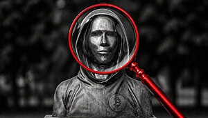 Das Bild zeigt eine Statue von Satoshi Nakamoto. Eine rote Lupe vergrößert das Gesicht.