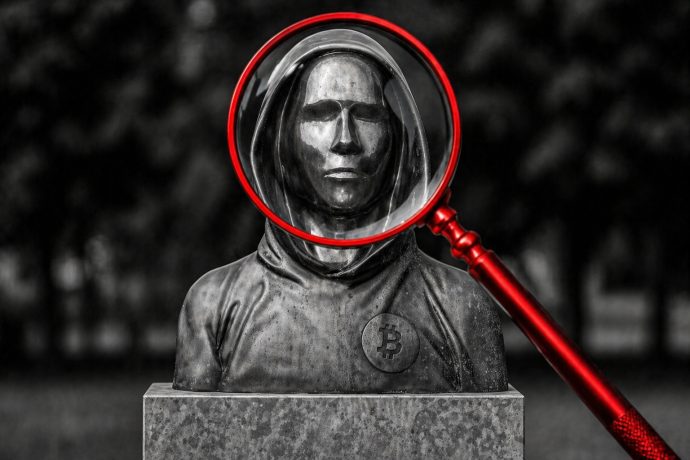 Das Bild zeigt eine Statue von Satoshi Nakamoto. Eine rote Lupe vergrößert das Gesicht.