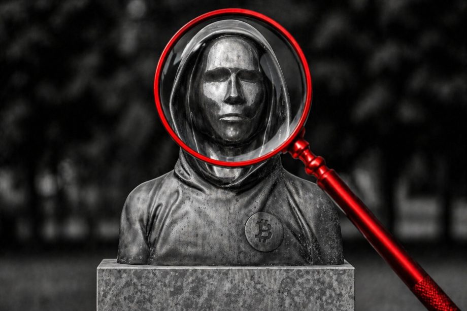 Das Bild zeigt eine Statue von Satoshi Nakamoto. Eine rote Lupe vergrößert das Gesicht.