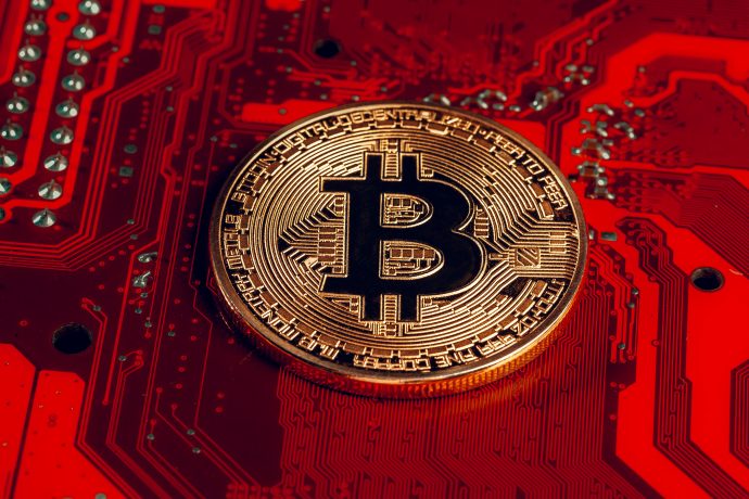 Eine Bitcoin-Münze liegt auf einem roten Computerchip