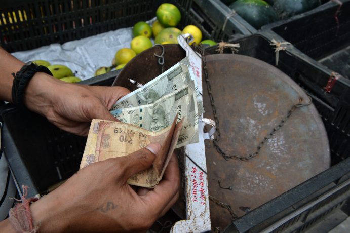 Jemand zählt indische Rupien vor einem Korb.