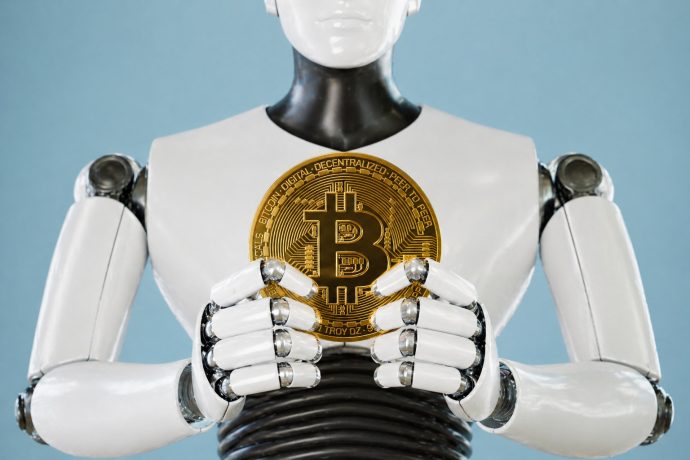 Ein humanoider Roboter hält mit seinen Händen eine Bitcoin-Münze vor eiem hellblauen Hintergrund.
