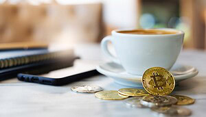 Ein paar Bitcoin-Münzen vor einer Kaffeetasse und einem Smartphone.