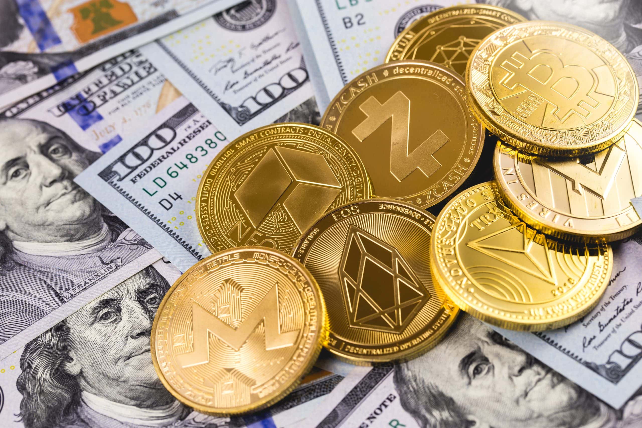 Ein Haufen verschiedener vergoldeter Altcoin-Münzen liegt auf mehreren US-Dollar-Noten.