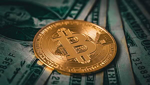 Eine vergoldete Bitcoin-Münze liegt auf verschiedenen US-Dollar-Noten.