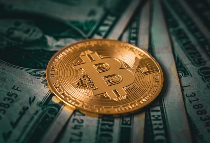 Eine vergoldete Bitcoin-Münze liegt auf verschiedenen US-Dollar-Noten.