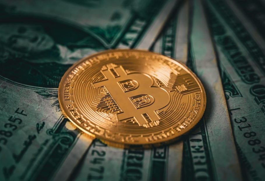 Eine vergoldete Bitcoin-Münze liegt auf verschiedenen US-Dollar-Noten.