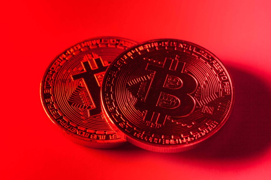 Zwei physische Bitcoin-Token (BTC) werden unter rotem Licht gezeigt, wobei auf ihrer Oberfläche kreislaufähnliche Muster zu erkennen sind, die das digitale Wesen von Bitcoin hervorheben.