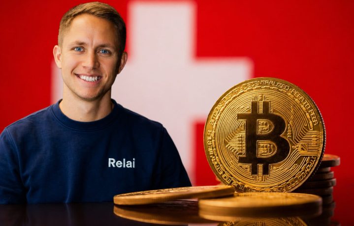Relai-CEO Julian Liniger steht links im Bild vor einer verschwommenen Schweizer Flagge und trägt einen dunkelblauen Relai-Pullover. Rechts daneben ist eine große goldene Bitcoin-Münze auf mehreren Coins zu sehen. Das Bild symbolisiert Bitcoin, die Schweiz und das Unternehmen Relai.