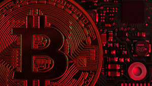 Eine stark vergrößerte Bitcoin-Münze ist vor einer elektronischen Leiterplatte zu sehen, wobei die Szene in rotes Licht getaucht ist und eine negative oder angespannte Marktsituation symbolisiert.