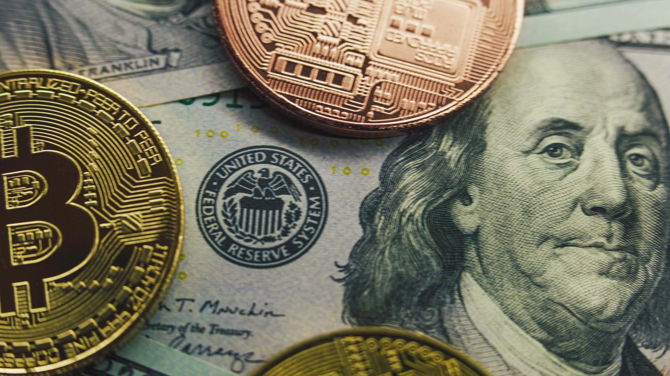 Im Hintergrund befinden sich US-Dollar-Banknoten. Im Vordergrund sind wiederum zwei Münzen abgebildet, die Bitcoin und eine andere Kryptowährung darstellen sollen.