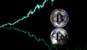 Eine Bitcoin-Münze steht im Vordergrund vor einem dunklen Hintergrund, während im Hintergrund ein aufwärts gerichteter Kurschart zu sehen ist, der sich in der Oberfläche spiegelt.