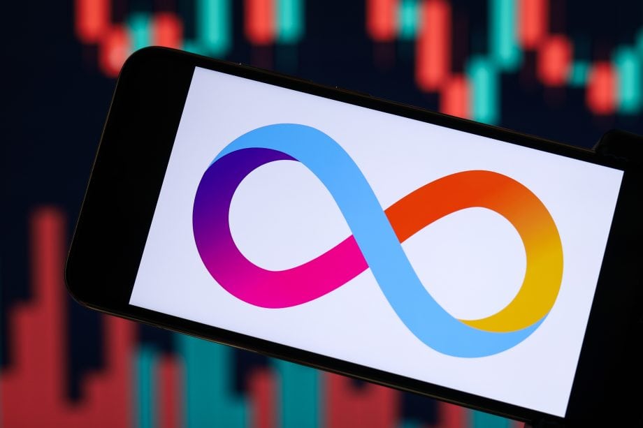 Zu sehen ist das Logo von Internet Computer (ICP) auf dem Display eines Smartphones. Im Hintergrund befinden sich unscharfe grün-rote Kurscharts, die auf die aktuelle Kursentwicklung und erhöhte Marktaktivität der Kryptowährung anspielen.