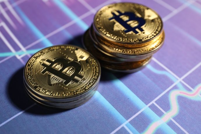 Zwei Bitcoin-Münzen liegen auf einem lila Chart-Hintergrund