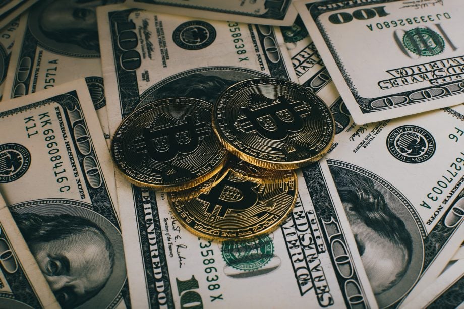 Das Bild zeigt eine Bitcoin-Münze auf Dollar-Scheinen