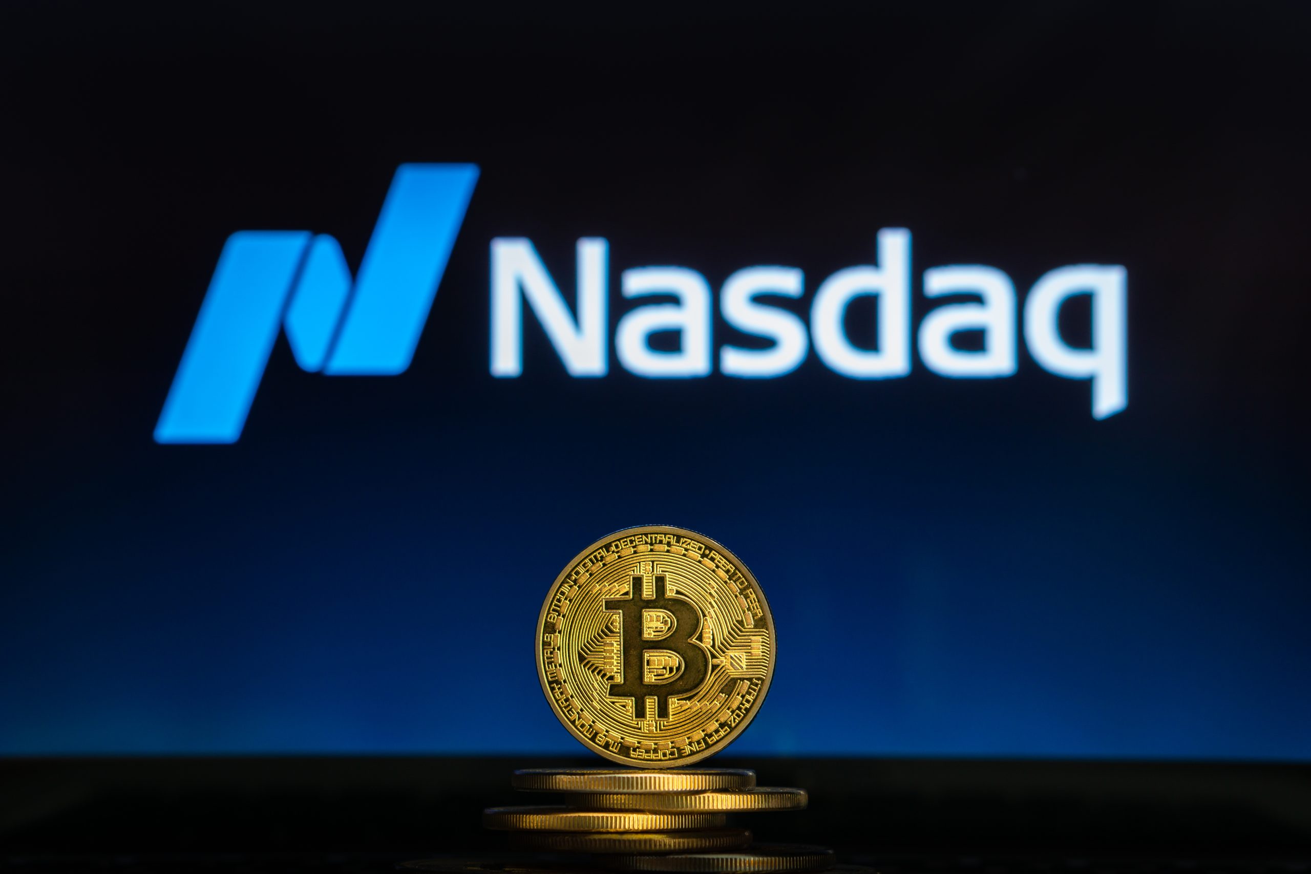 Das Bild zeigt eine Bitcoin-Münze mit dem Nasdaq-Logo