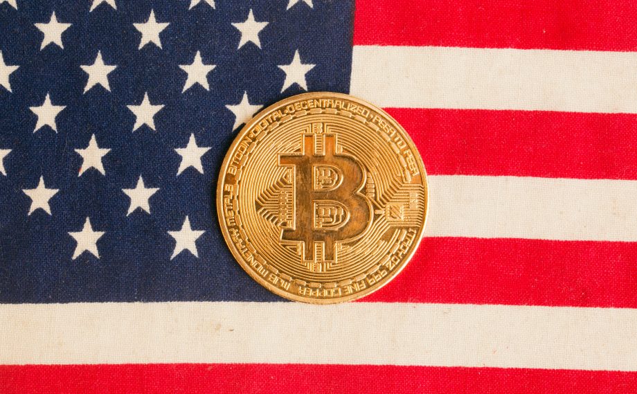 Man sieht die USA-Flagge und in der Mitte ist eine goldene Bitcoin-Münze platziert.