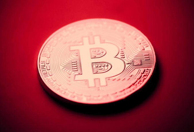 Wie weit sinken die Bitcoin ETFs noch? Eine Bitcoin-Münze vor einem roten Hintergrund