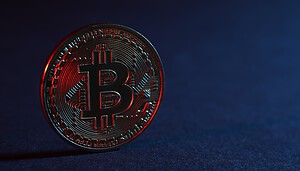Bitcoin-Münze schimmert rötlich vor einem dunkelblauen Hintergrund.