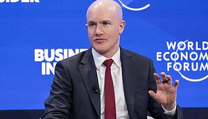 Ein Mann im Anzug und mit roter Krawatte spricht während einer Podiumsdiskussion auf dem Weltwirtschaftsforum, im Hintergrund sind blaue Banner und das Coinbase-Logo zu sehen.