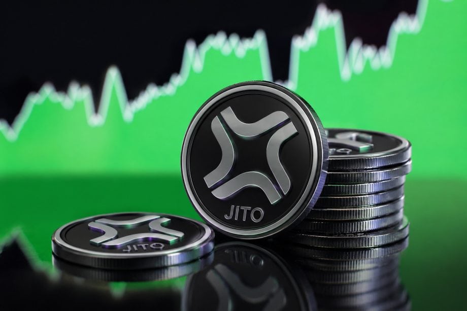 Mehrere metallische Jito-Token liegen auf einer glänzenden, spiegelnden Oberfläche. Im Vordergrund steht ein großer Jito-Token, daneben befindet sich ein Stapel weiterer Token. Im Hintergrund zeigt ein unscharfer grüner Kurschart mit aufsteigender Tendenz eine positive Marktentwicklung. Die Szene vermittelt das Thema Kryptowährungen, Investment und Kurswachstum.