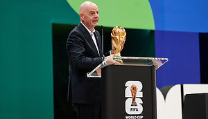 FIFA-Präsident Gianni Infantino hält den WM-Pokal vor einem Podium.
