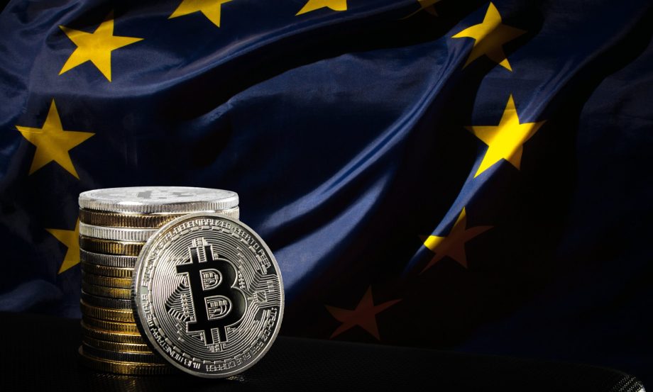 Stapel physischer Bitcoin-Münzen vor einer entfalteten Flagge der Europäischen Union, die den Markteintritt von Coinmerce in Deutschland und die Bereitschaft für die kommenden MiCAR-Lizenzbestimmungen symbolisiert.