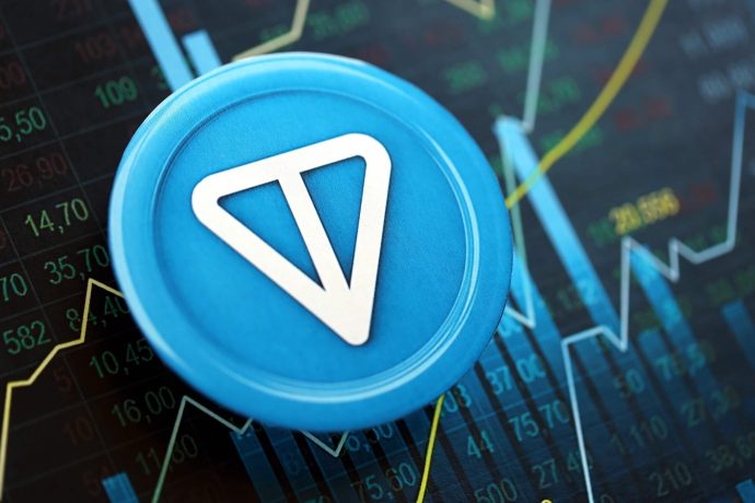 Eine Münze mit Toncoin-Logo liegt auf einem blau gefärbten Kurschart