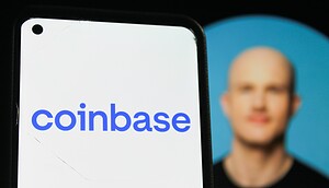 Das Bild zeigt im Vordergrund ein Smartphone mit dem Coinbase-Logo auf dem Display. Im unscharfen Hintergrund ist Coinbase-CEO Brian Armstrong vor einem blauen Hintergrund zu sehen. Durch die geringe Tiefenschärfe liegt der Fokus klar auf dem Unternehmenslogo.