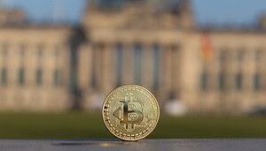 Eine Bitcoin-Münze vor einem verschwommenen Bild des Deutschen Bundestags.