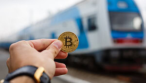 Das Bild zeigt eine Bitcoin-Münze vor einem Zug