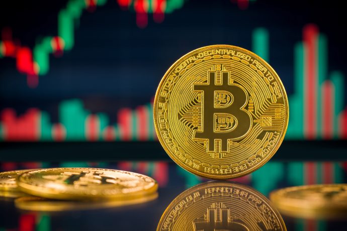 Eine Bitcoin-Münze vor einem Kurschart.