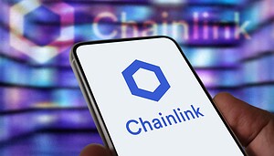 Das Bild zeigt ein Smartphone mit dem Chainlink-Logo auf dem Display. Im unscharfen Hintergrund ist ebenfalls das Chainlink-Branding zu erkennen. Die Aufnahme visualisiert das Blockchain-Projekt und dessen Rolle als Infrastrukturanbieter im Krypto- und Finanzsektor.