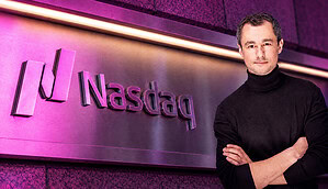 Das Logo der Nasdaq wird violett angeleuchtet. Rechtbündig steht ein Mann mit einem schwarzen Rollkragenpullover.